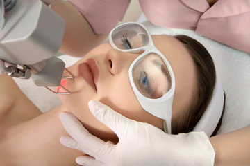 Lady on medical table with self protective eyewear having a laser facial procedure with medically gloved hands positioning her face