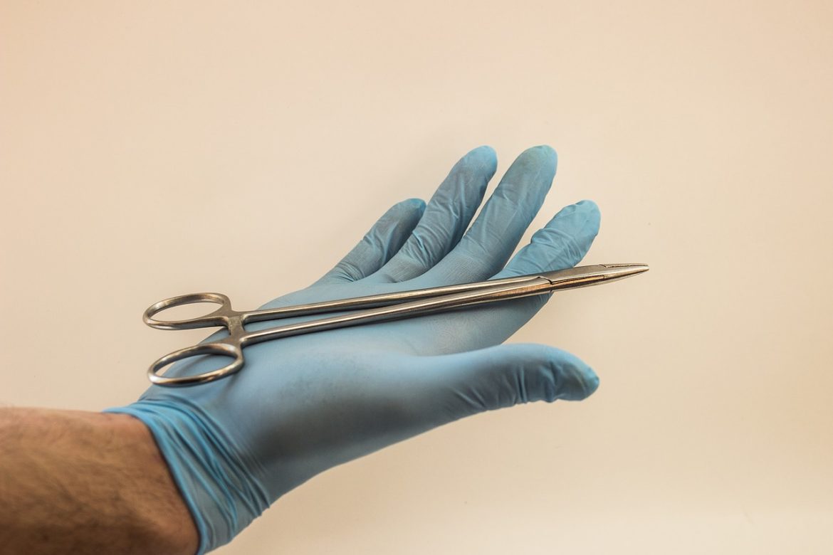 A blue gloved hand holding medical scissors