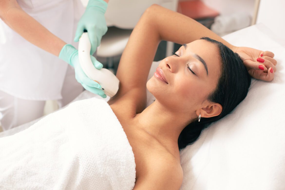 Calm young woman lying with closed eyes and putting on arm up while having laser hair removal procedure